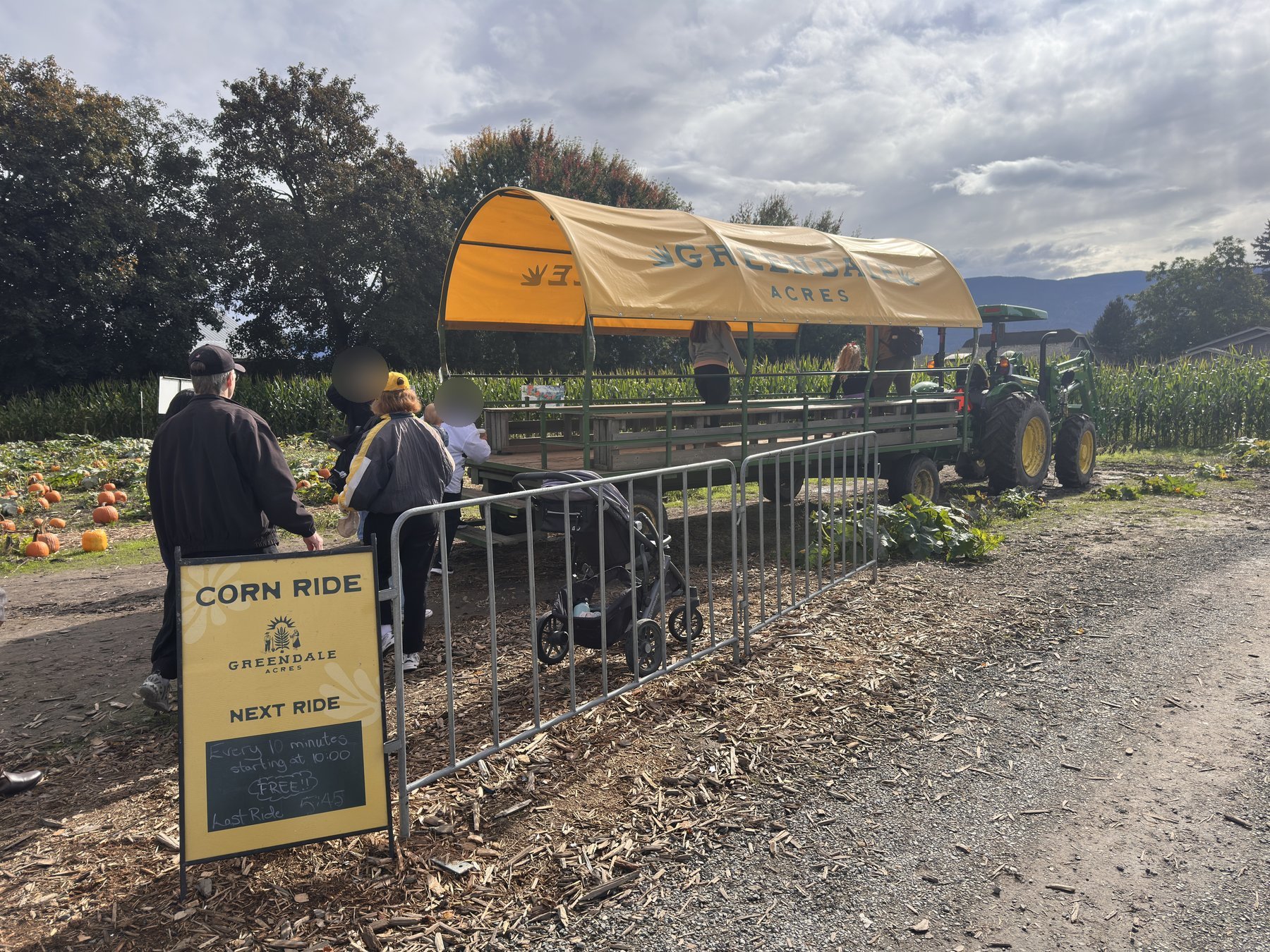 Covered yellow Greendale Acres hay wagon behind a green tractor, with a "Corn Ride – Free" sign