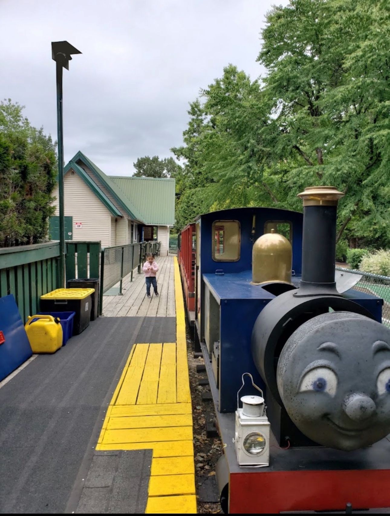 Friendly blue Eddy the Engine miniature train stopped at the Bear Creek Park station platform under evergreen trees.