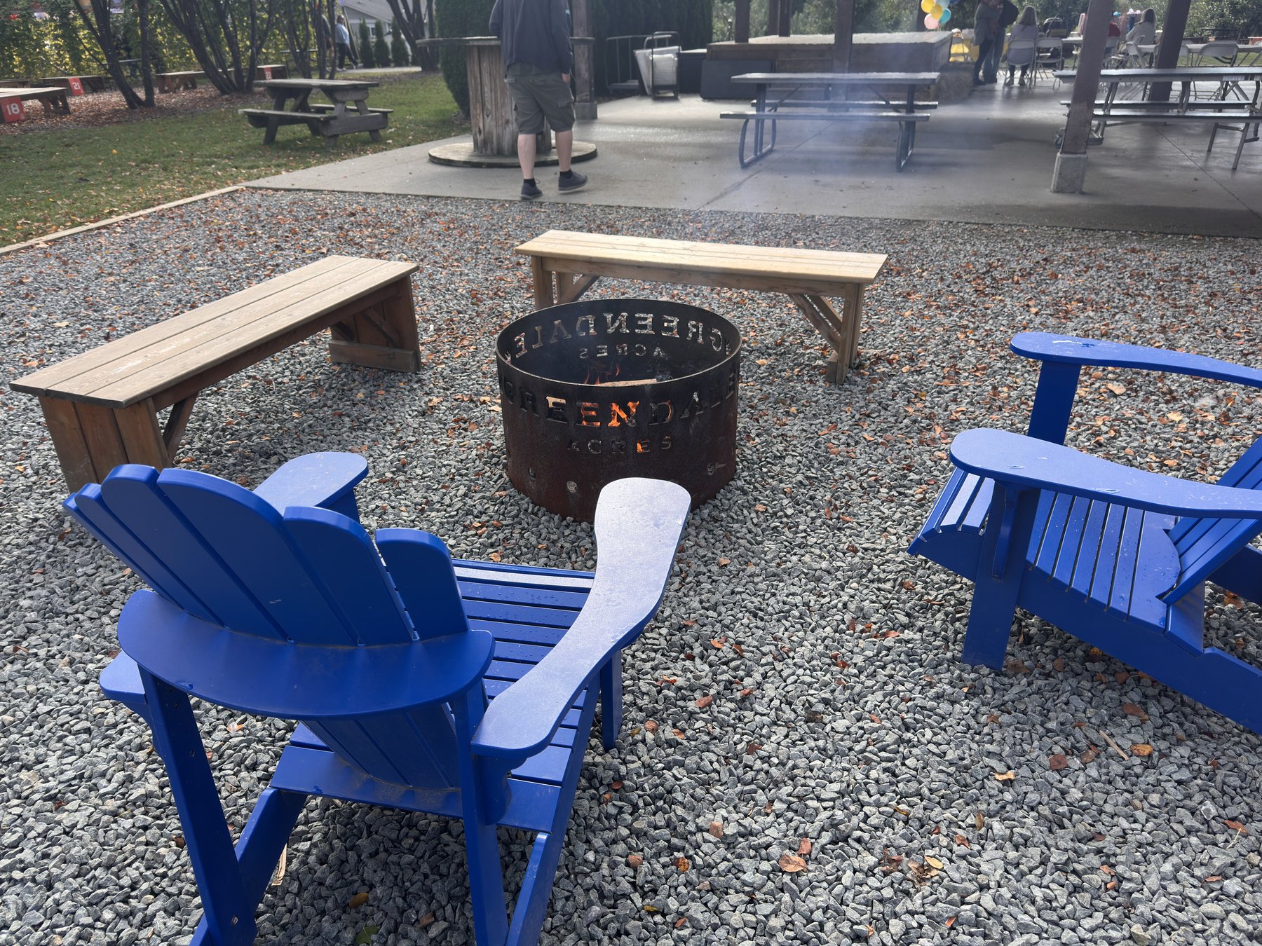 Metal Greendale fire pit ring with blue Adirondack chairs and wooden benches