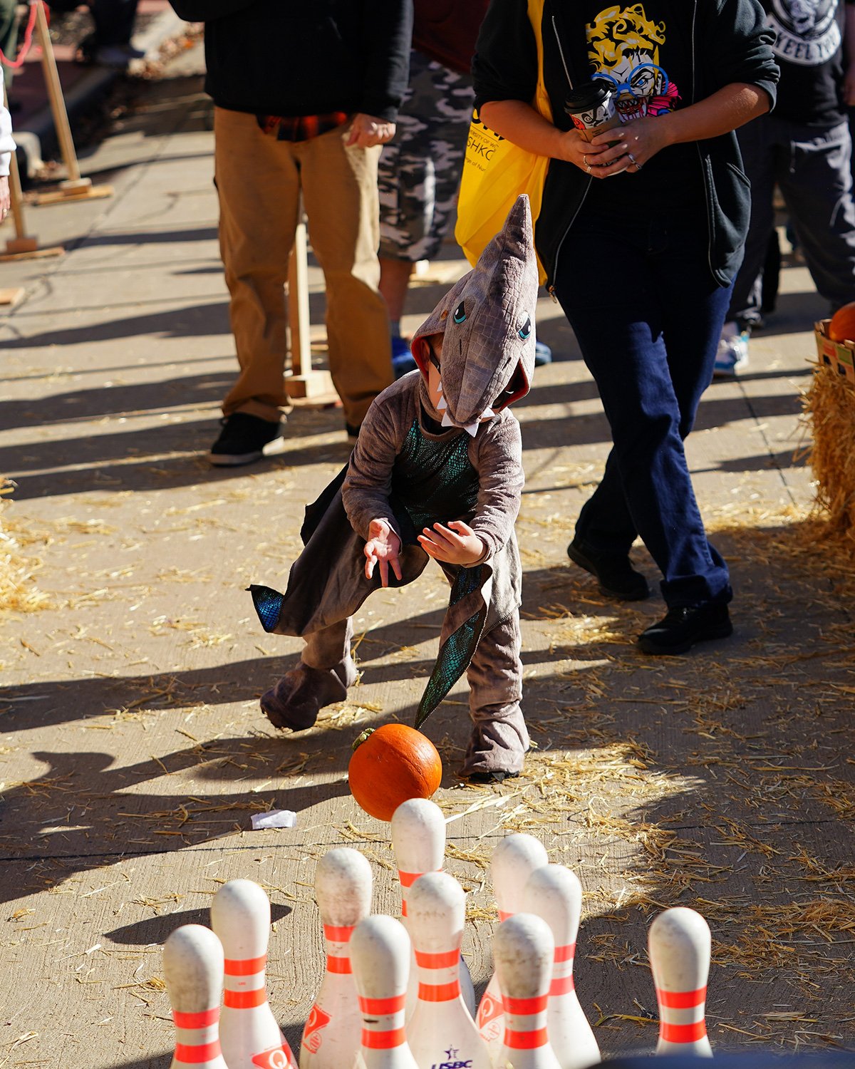 Child in a shark costume bowling a small pumpkin at pins