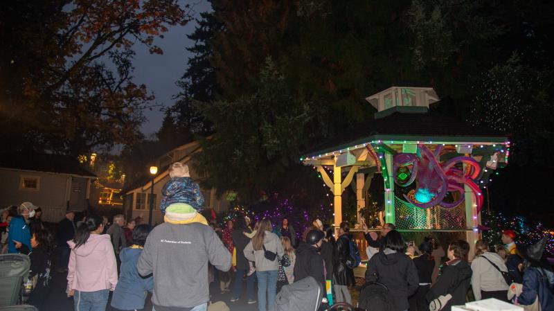 Crowds around the lit-up bandstand at Haunted Village, Burnaby Village Museum